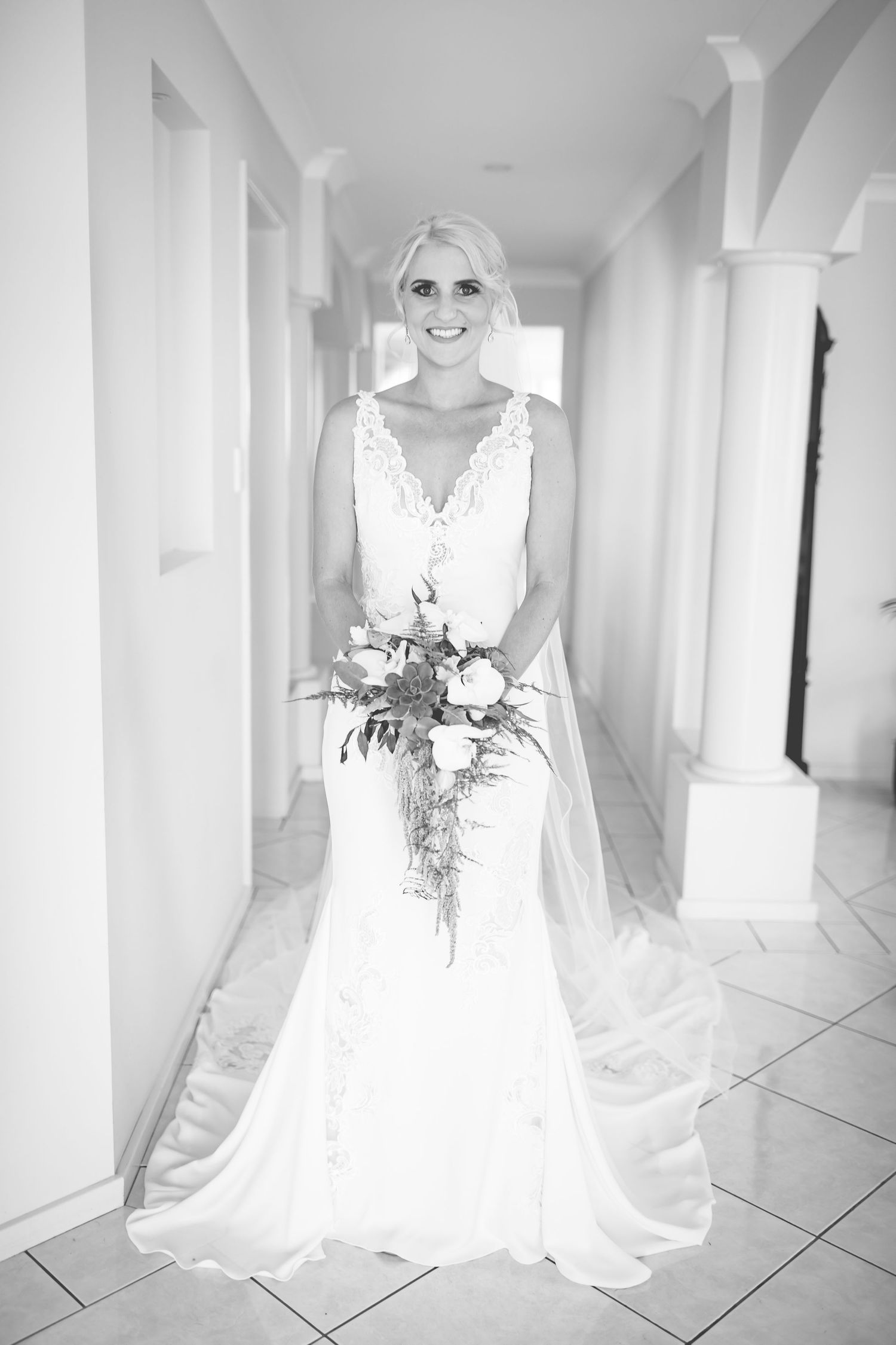 Elegant bridal portrait in white lace gown with cascading bouquet in bright hallway.