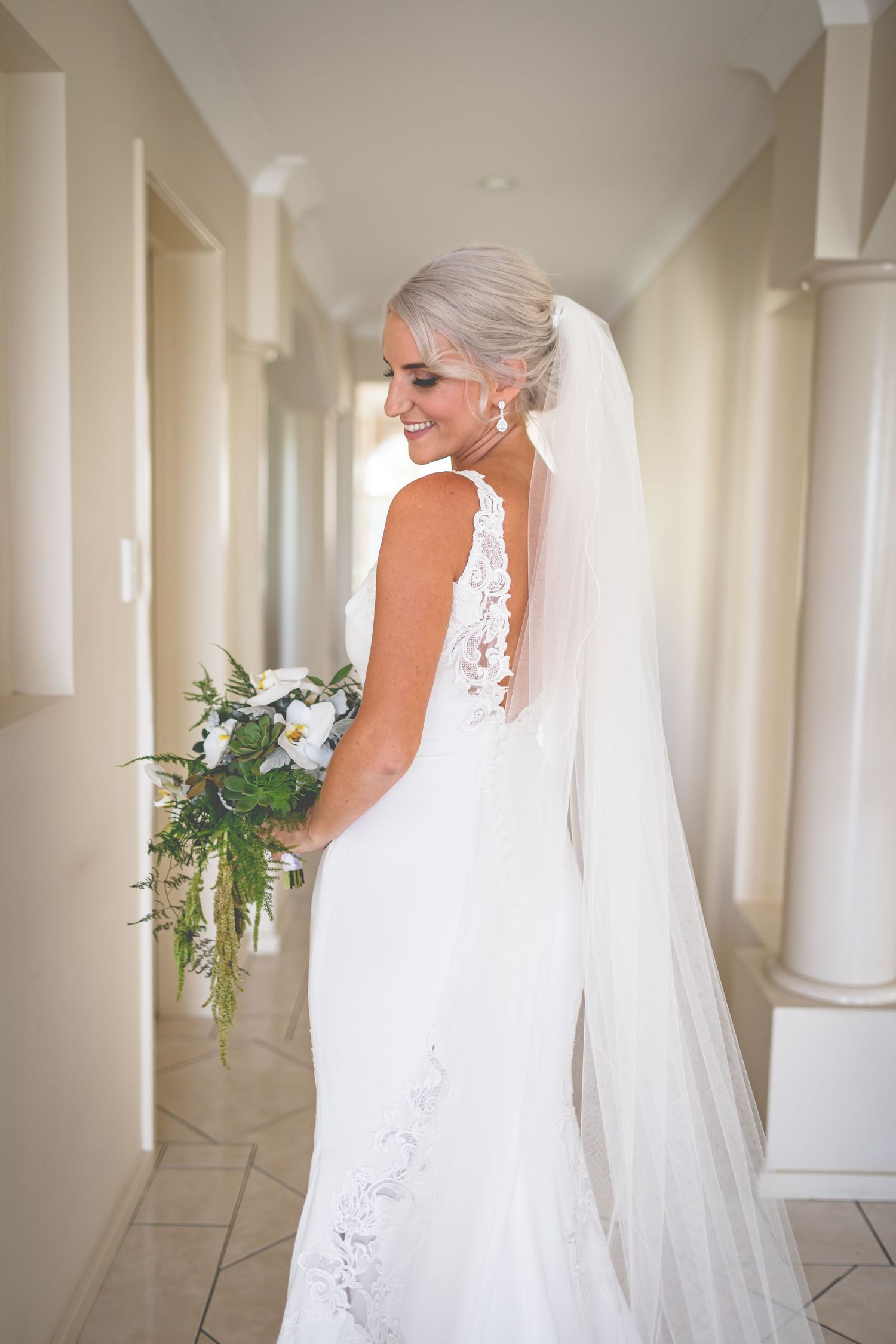 Side view bridal portrait showcasing lace back detail and flowing veil in sunlit corridor.