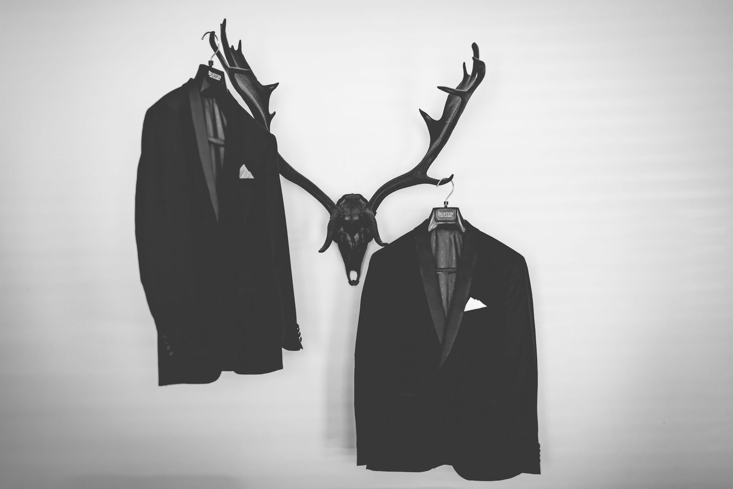 Artistic black and white photo of suit jackets hanging with antler decor.