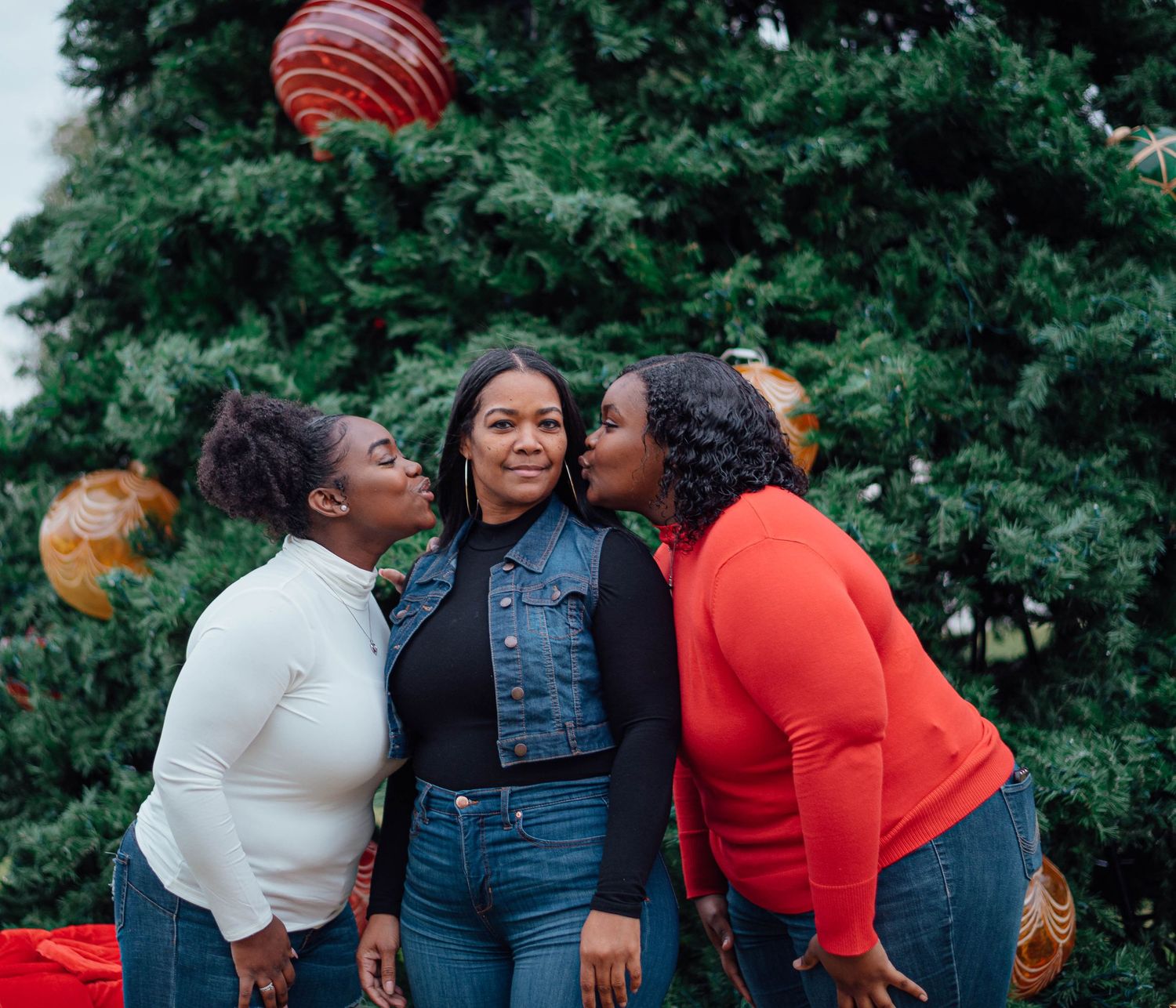 Three friends sharing a joyful moment in front of a Christmas tree with red and gold ornaments.