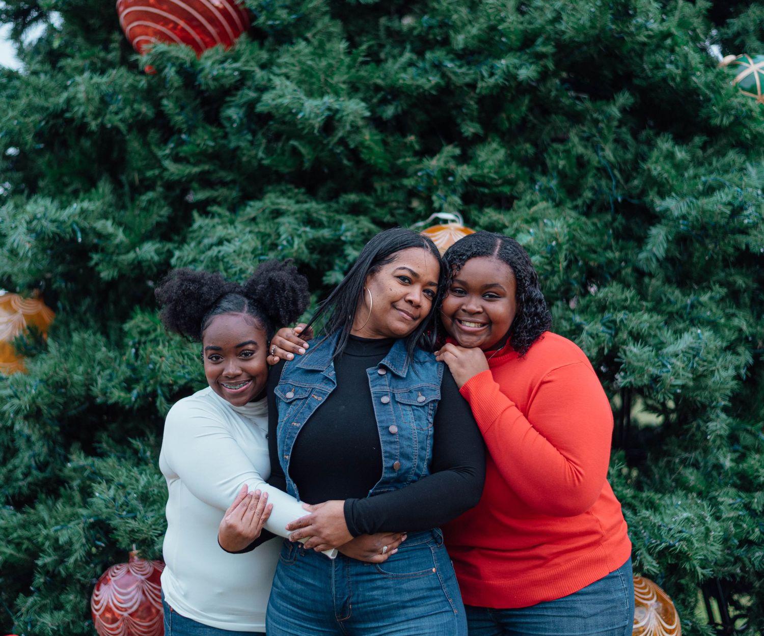 Friends laughing and hugging while posing for a photo in front of a decorated Christmas tree.