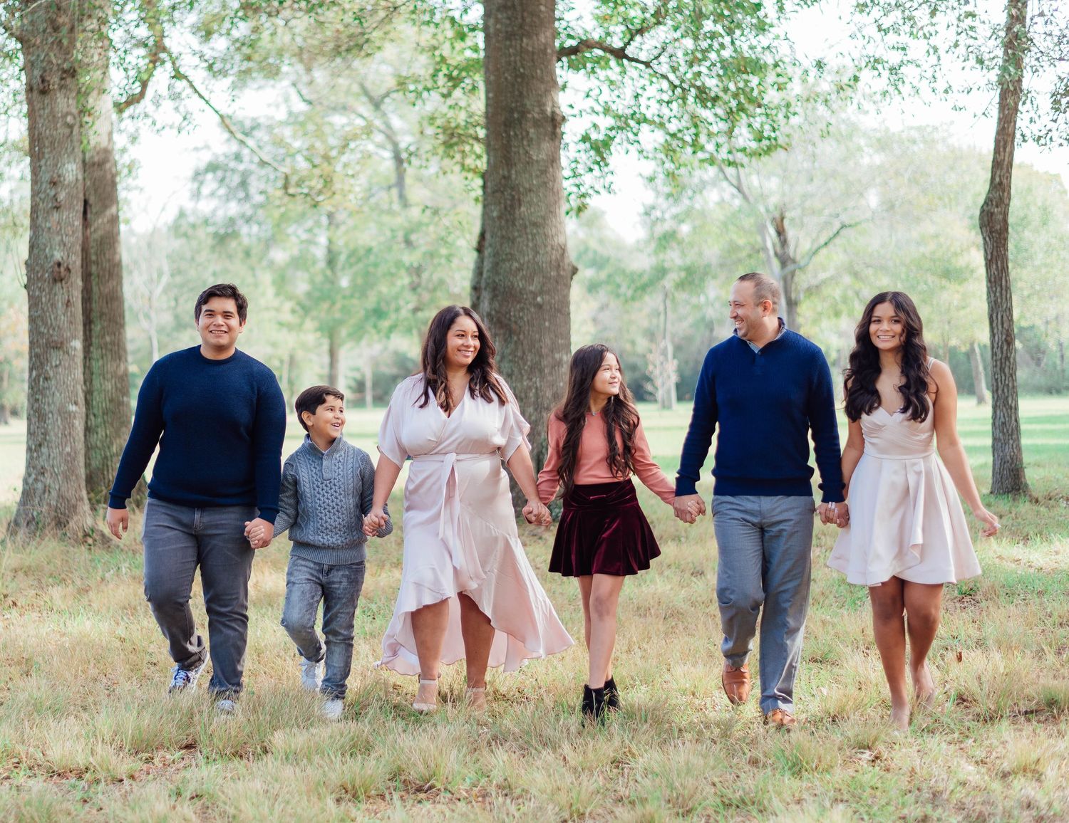 Family of six walking together through a wooded park setting in coordinated outfits.