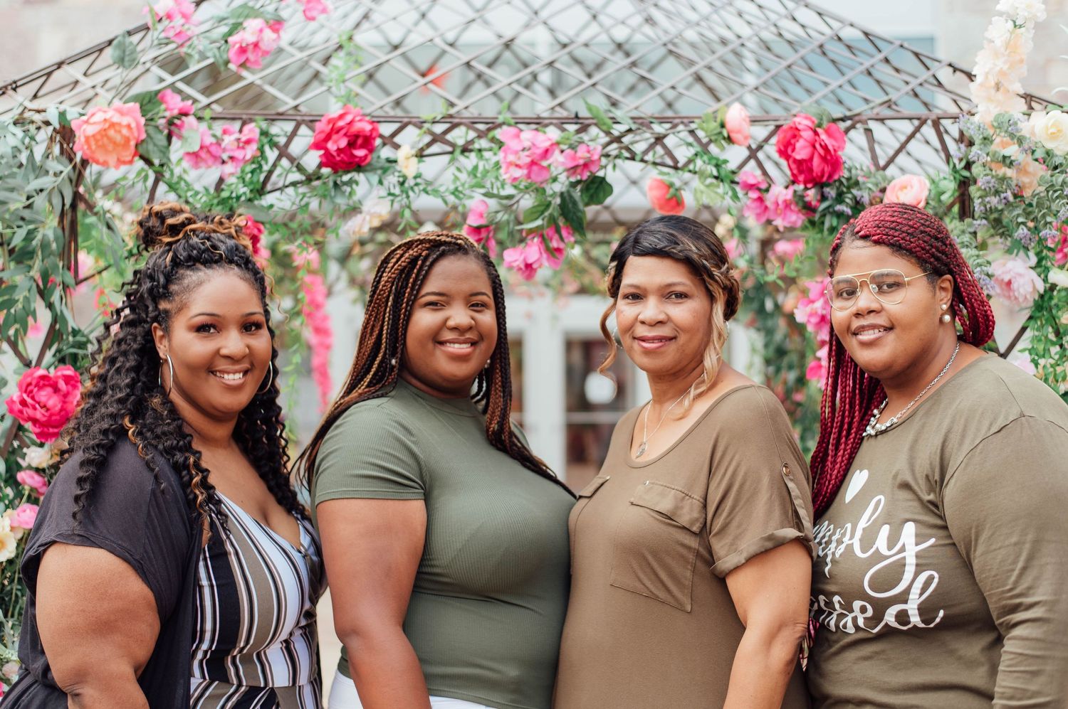 Four friends pose together under a beautiful rose-covered arch during an outdoor photoshoot.
