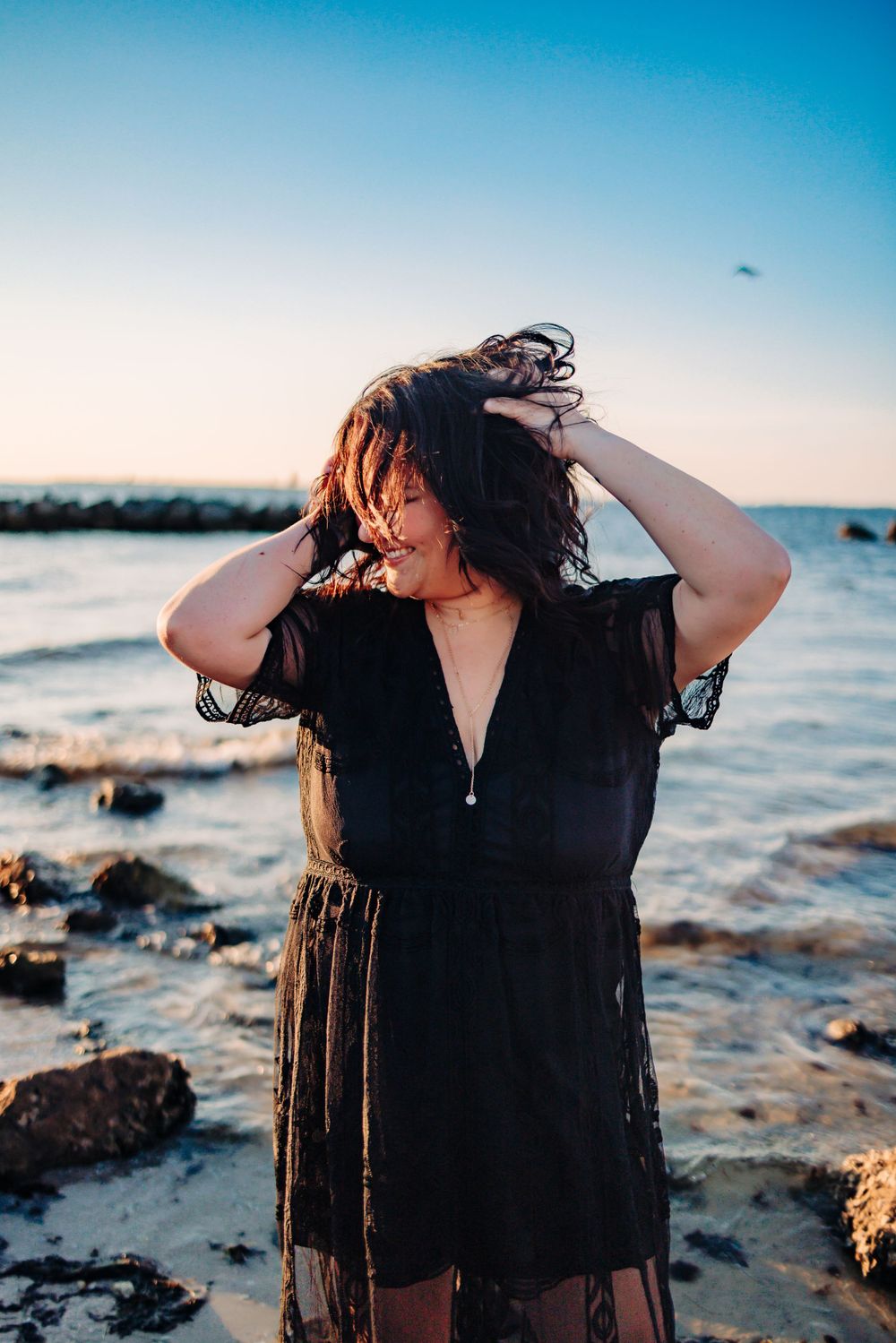 Dramatic beachside portrait with black sheer dress against ocean backdrop.