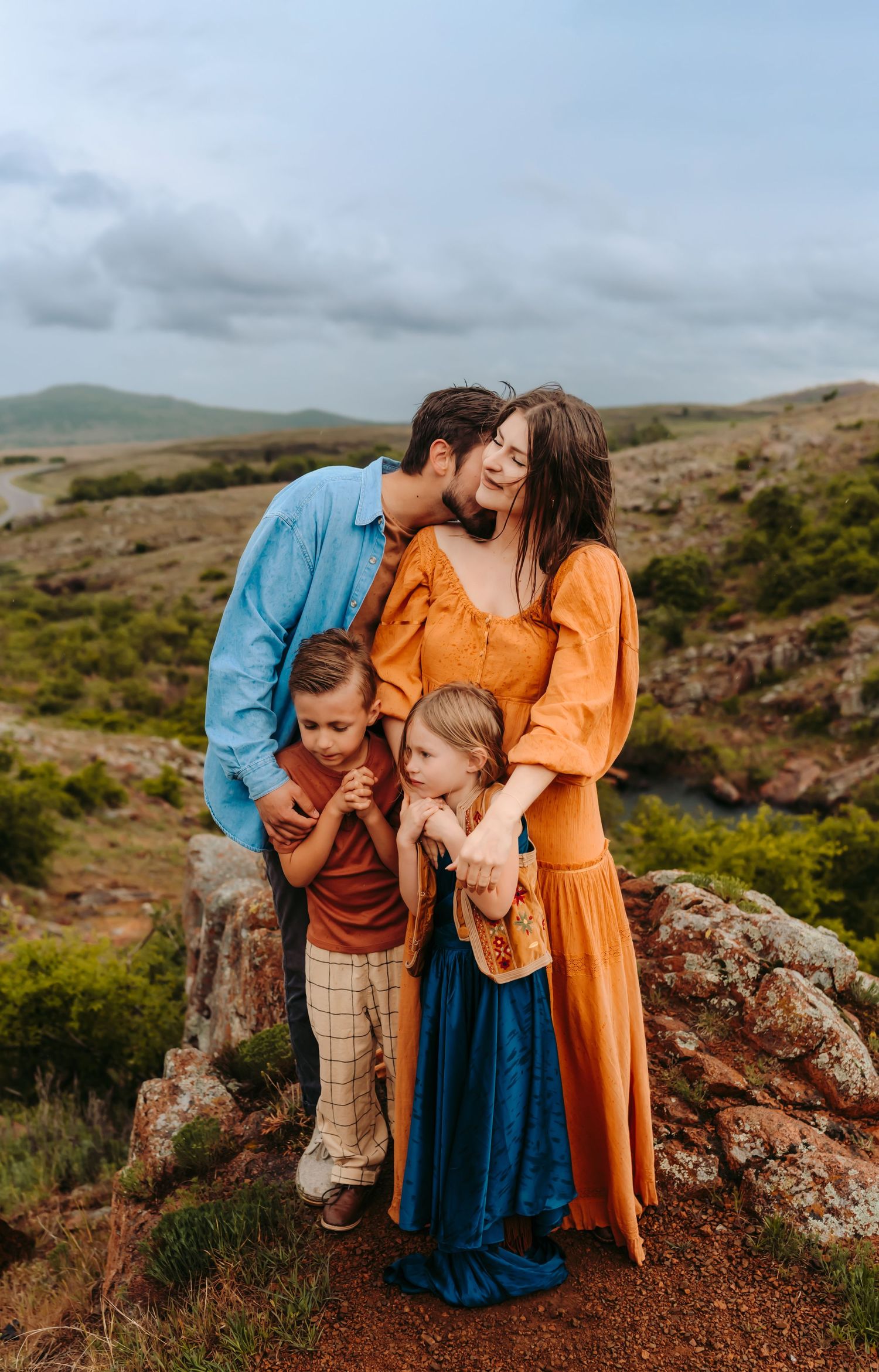 Family of four posing together on a rocky hillside with a scenic landscape in the background.