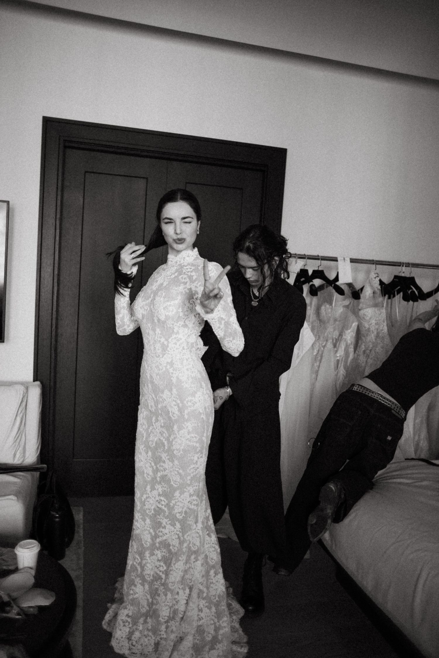 Elegant lace wedding gown being fitted in a dressing room with bridal preparations underway.
