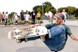 Skateboarder performing a trick in overalls at a skate park with spectators in the background.