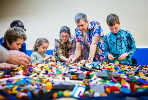 Group of people enthusiastically sorting through colorful LEGO bricks on a table.