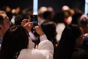 Person taking a photo in a crowded dark audience setting.