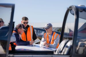 Aviation staff in high visibility vests review paperwork near parked aircraft.