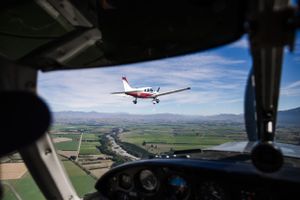 View from cockpit shows another small aircraft flying over rural landscape.