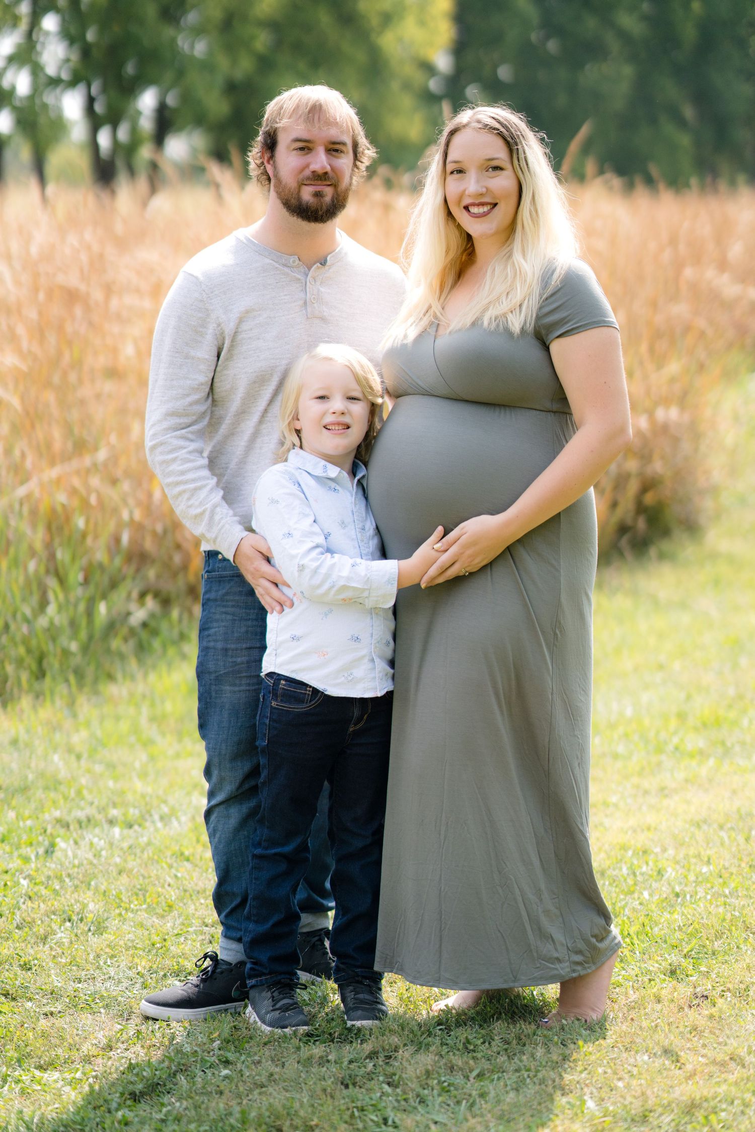 A family maternity photoshoot in a grassy field during golden hour.