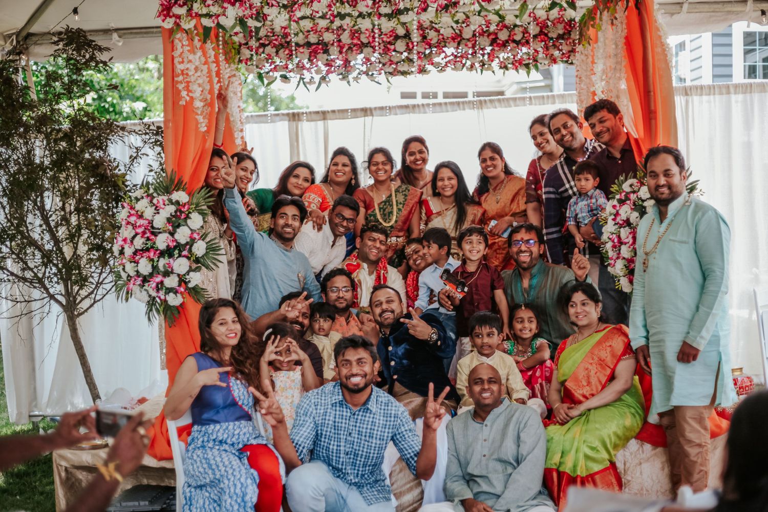 Large group photo of wedding guests gathered under floral decorations at an outdoor celebration.