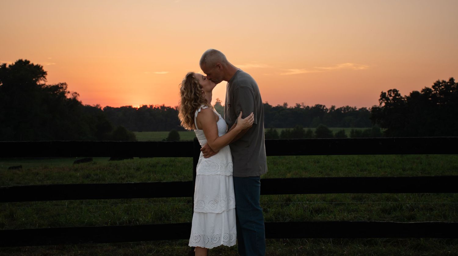 A romantic silhouette of a couple embracing at sunset against a rural landscape.