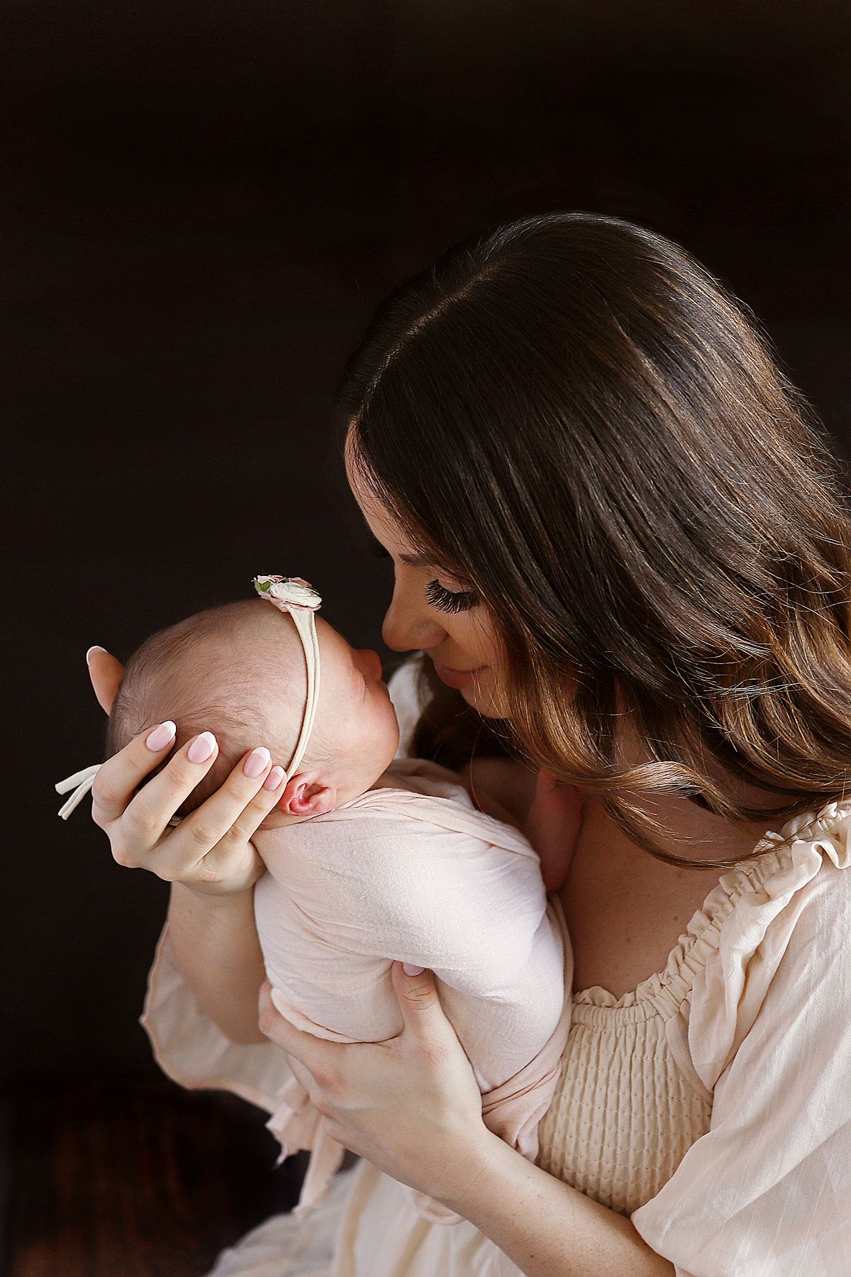 Intimate portrait showing tender moment with infant in soft lighting against dark background.