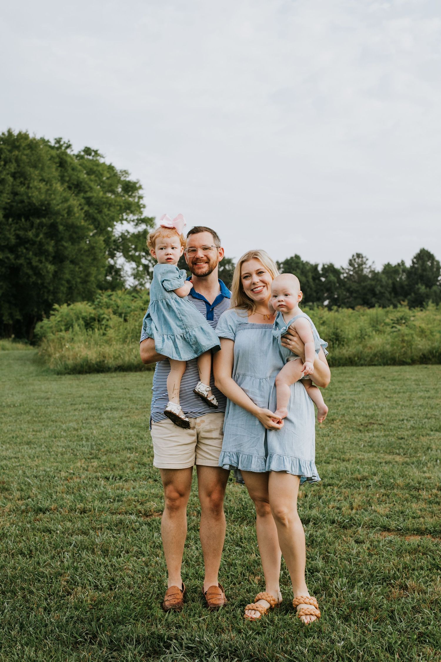 Family in coordinating blue outfits poses together on grassy hill.