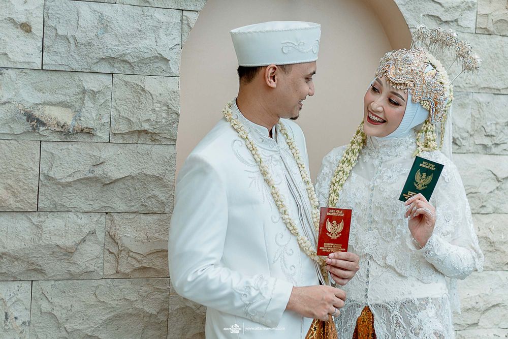 Indonesian newlyweds showing their marriage documents in traditional wedding attire.