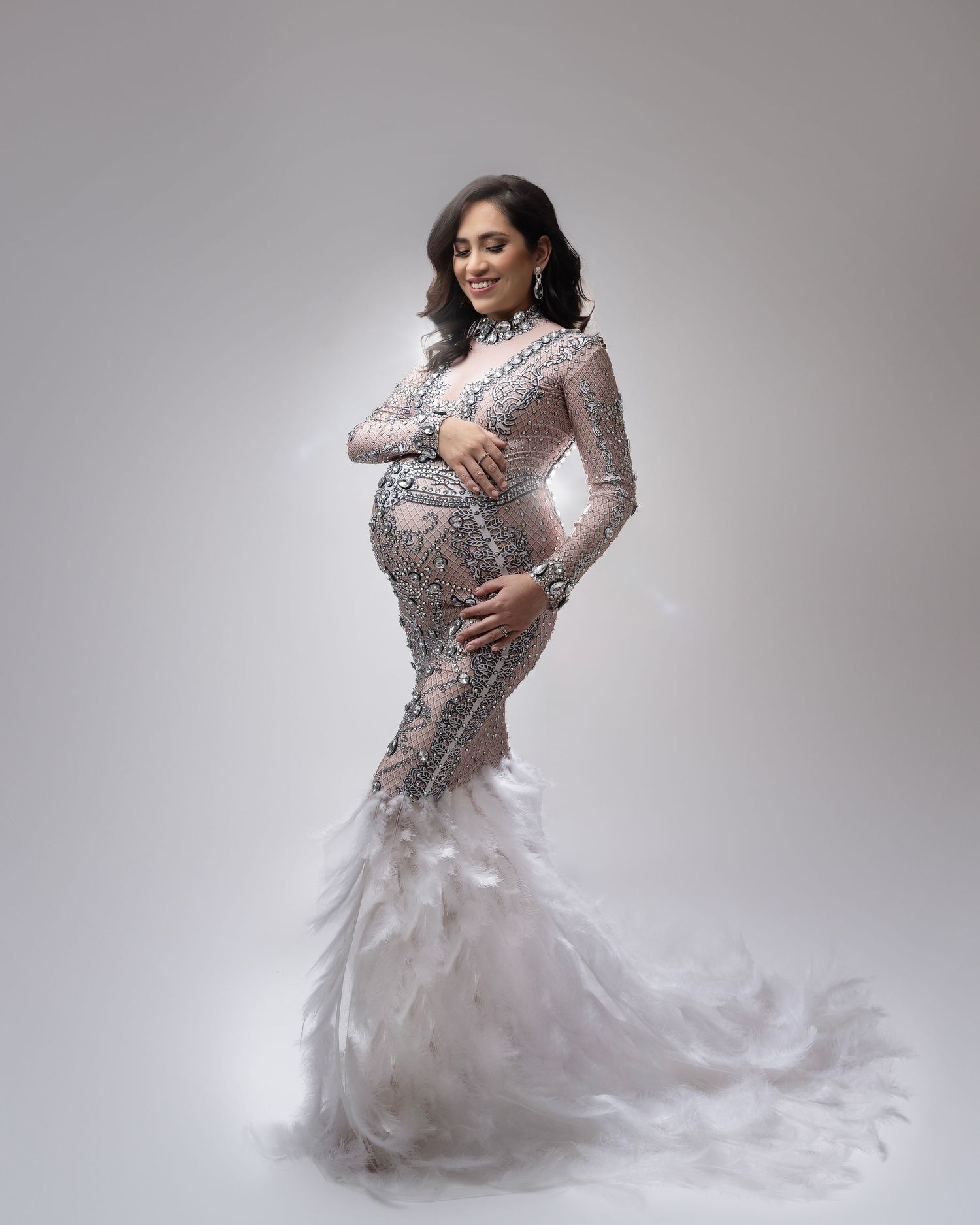 Studio maternity portrait in silver beaded gown with white feather details.