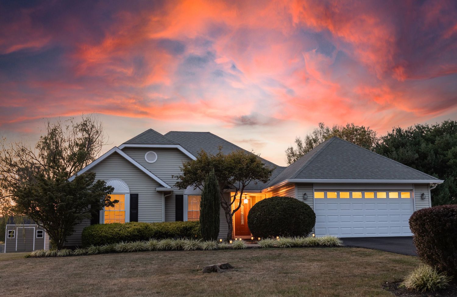 Single-story home with white garage door at sunset with dramatic orange and pink sky.