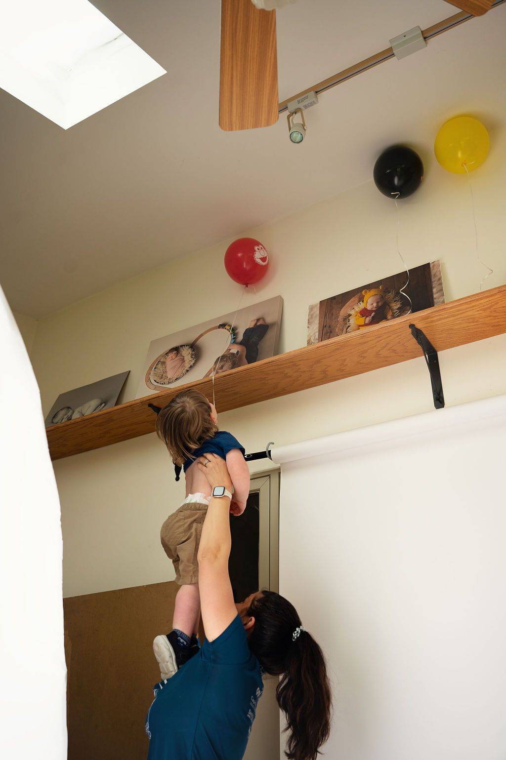 Two people working together to reach high shelf with colorful balloons decorating the wall.