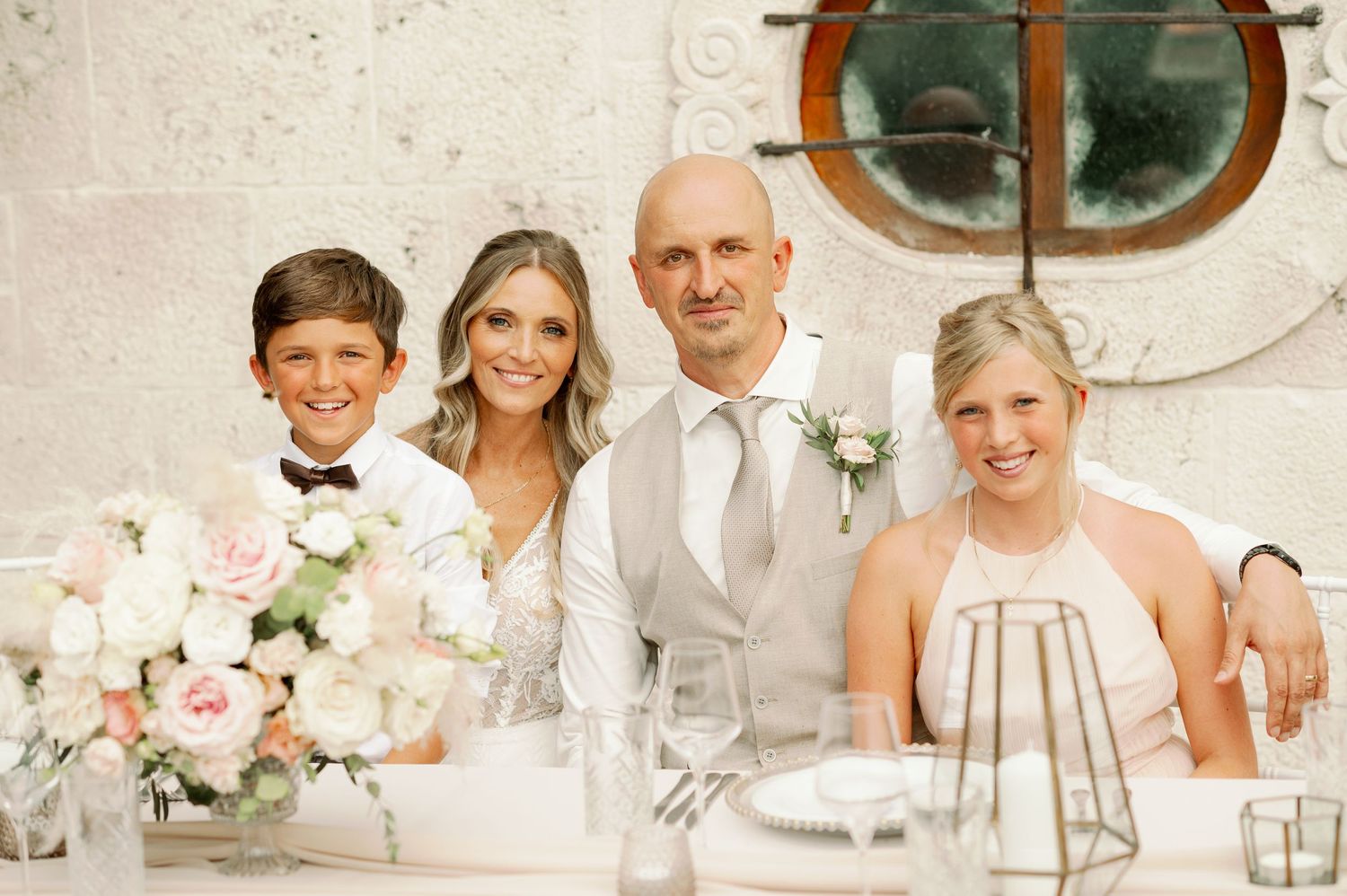 Wedding party seated at elegant reception table with vintage porthole window.