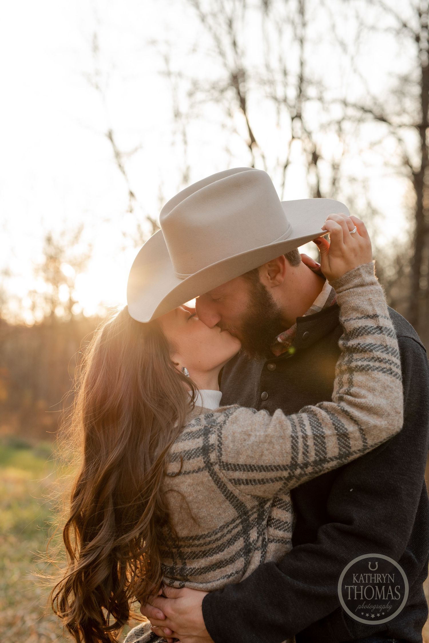 A romantic sunset moment between a couple in a field as they share a cowboy hat.