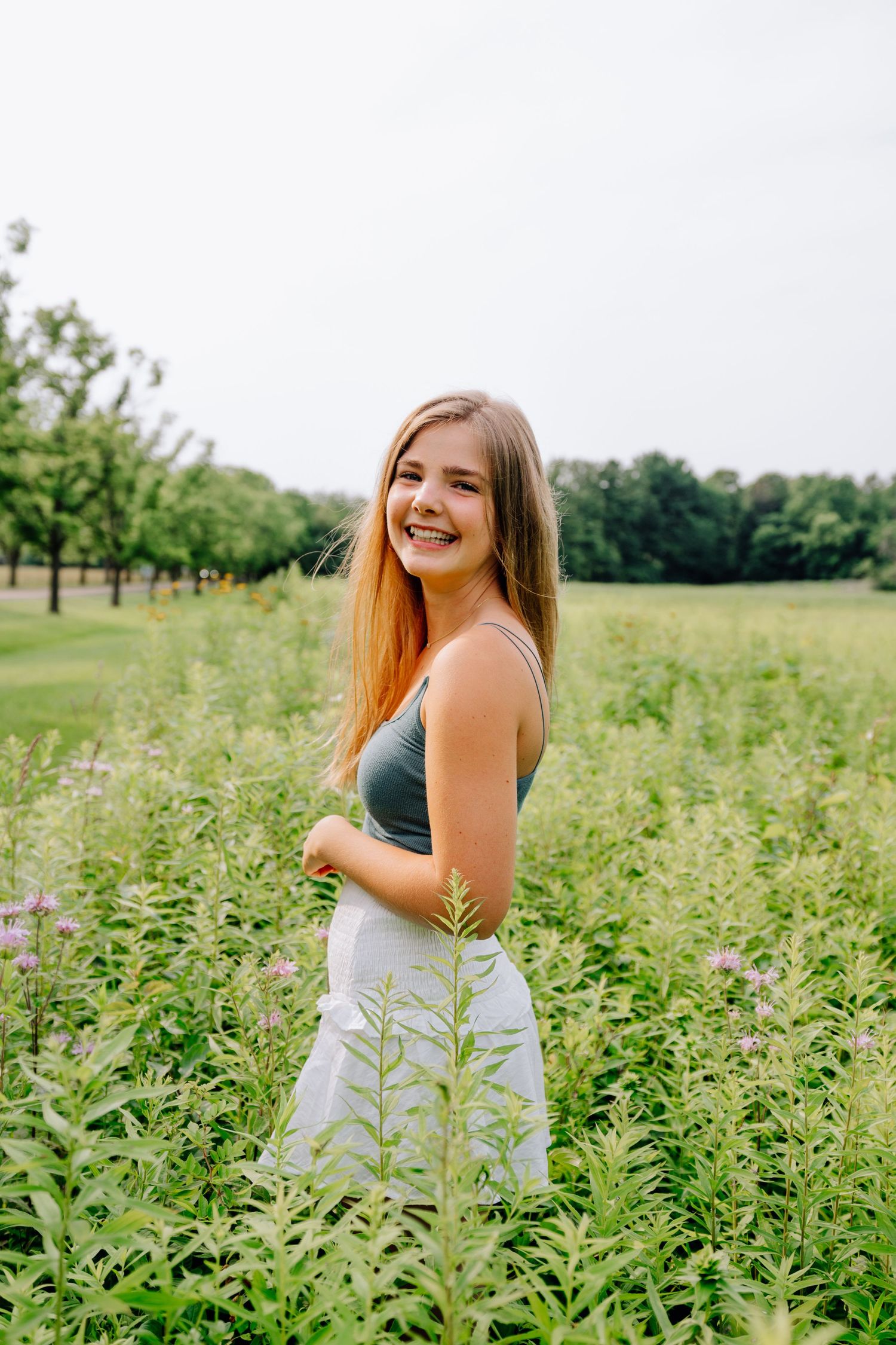 Person in light colored dress poses playfully in field of flowering plants.