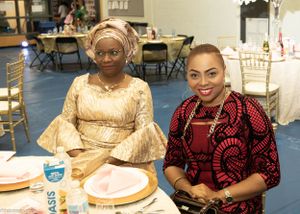 Two guests in traditional African attire seated at a formal dinner table with plates and drinks.