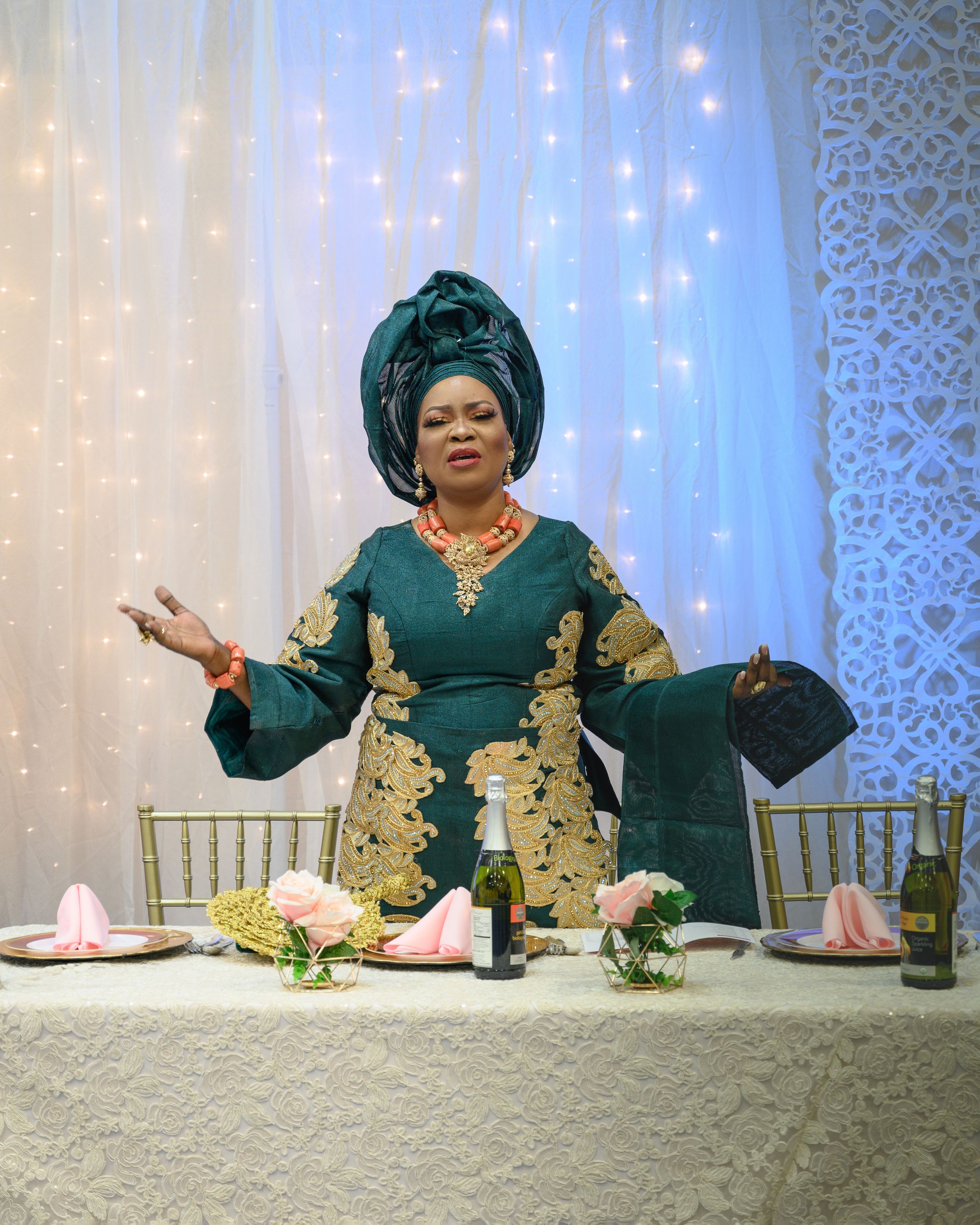 Woman in emerald green and gold traditional dress seated at decorated dining table.