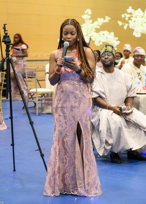 Young woman in a pink evening gown performs on stage with traditional decor and audience.