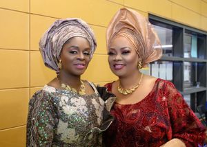 Two guests in elaborate Nigerian-style gowns and headwraps at formal celebration.