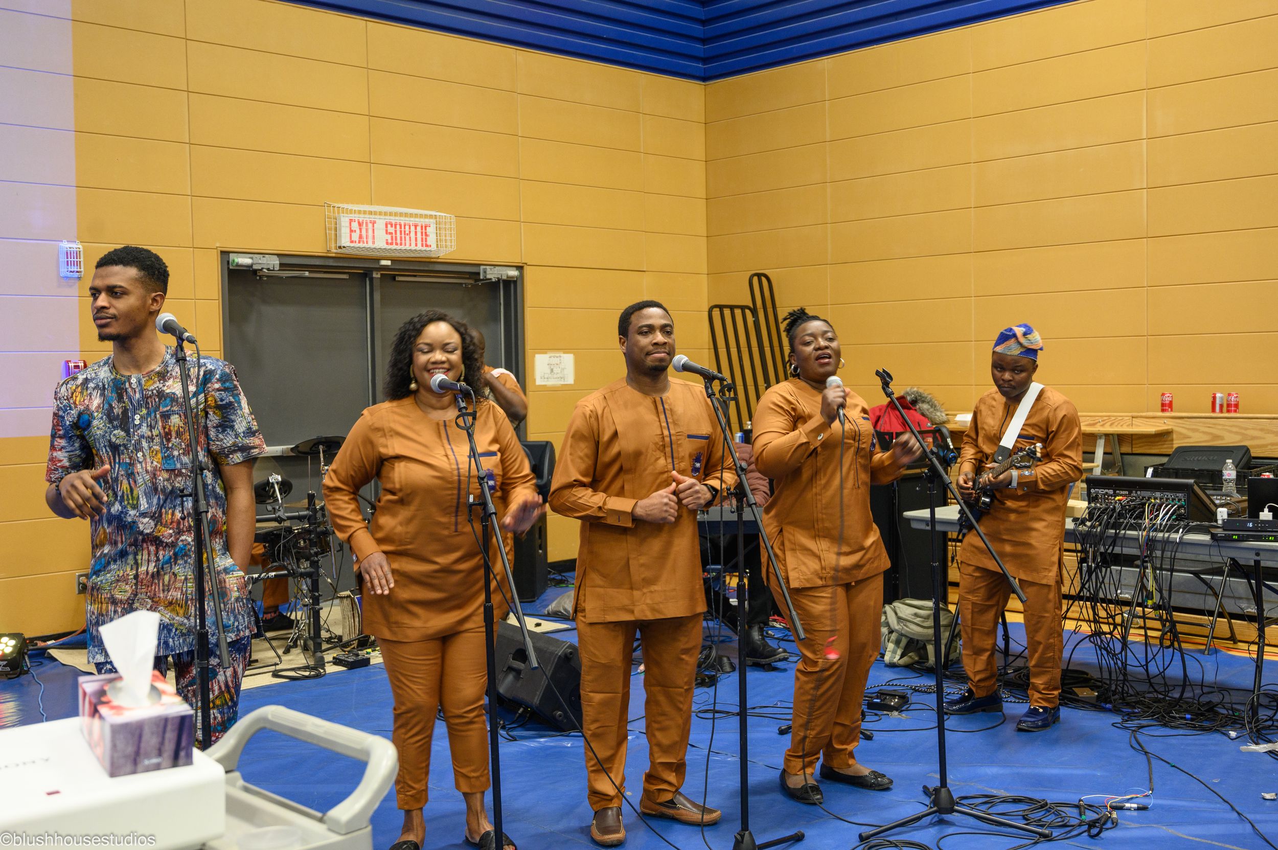 Band performing in matching brown outfits on stage in gymnasium setting.