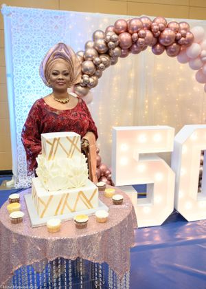 An elegant 50th birthday celebration featuring a white geometric cake under a balloon arch.