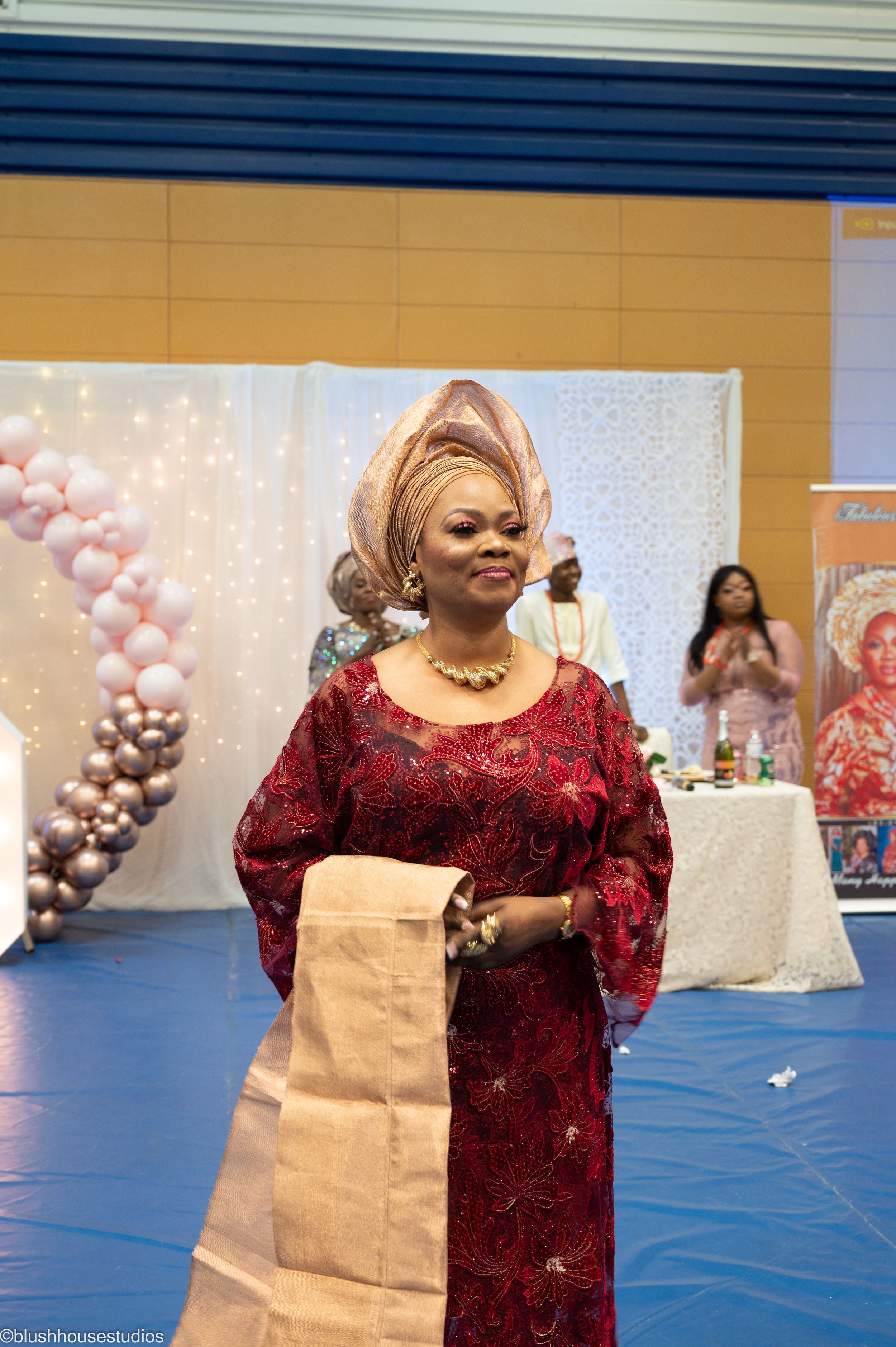 A performer in traditional Nigerian attire singing at a celebration with balloon decorations.