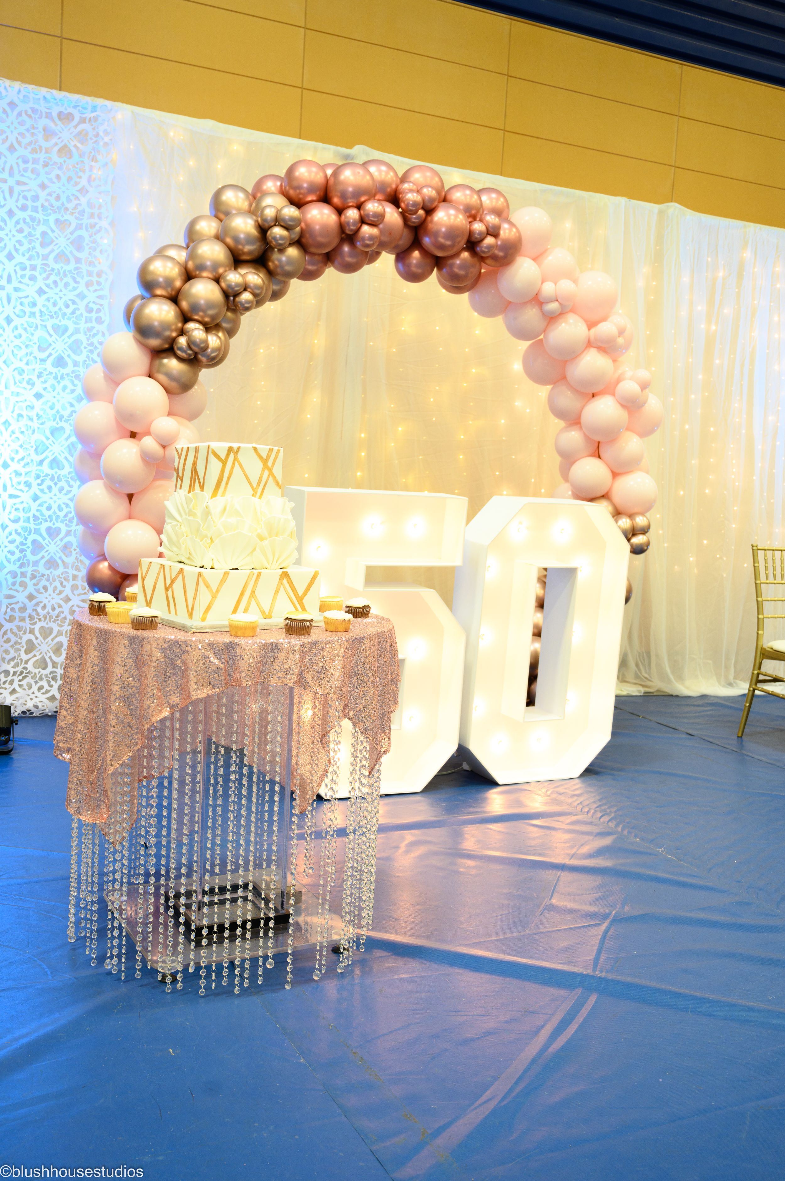Elegant 50th birthday party decor with rose gold balloon arch and crystal-draped cake table.