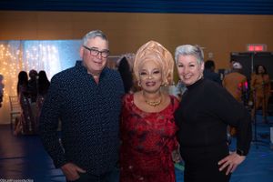 Three people posing together at an event with decorative lighting in the background.
