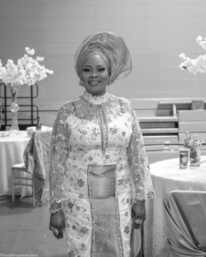 Person wearing an elegant floral embroidered dress and traditional headwrap at a formal event with table decorations.