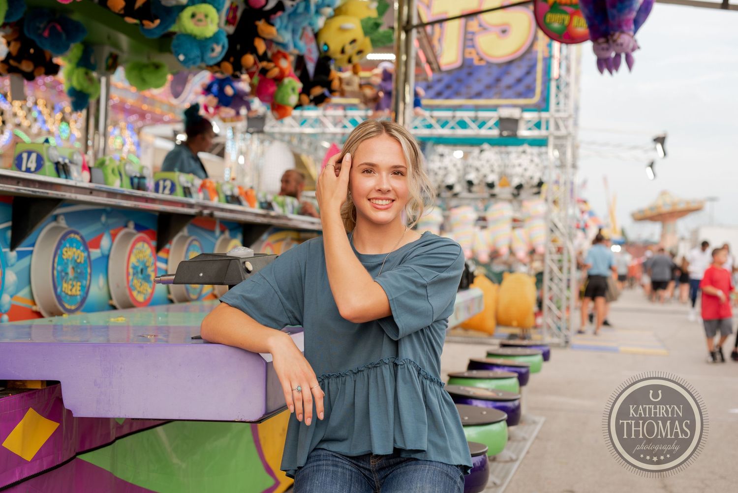 Person leaning against colorful carnival game booth wearing casual blue top.