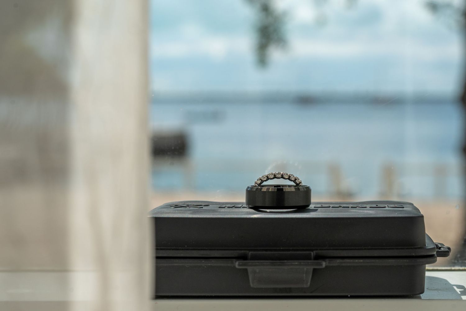 A black camera case sits on a table with water view visible through window.