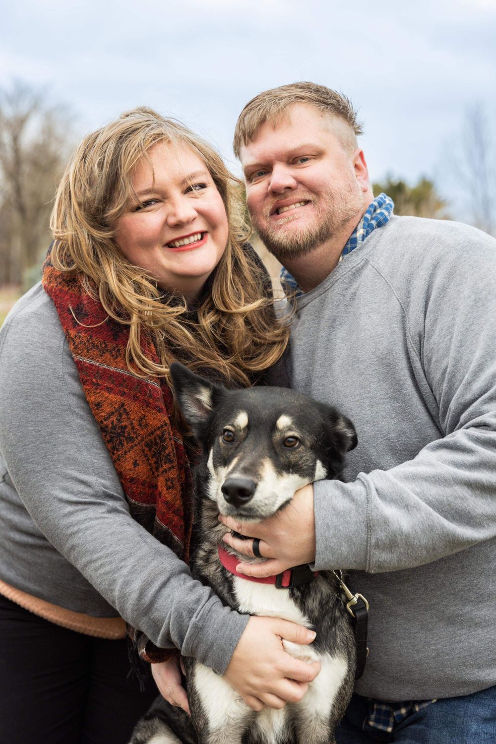 Happy couple cuddles with their black and white husky dog during outdoor photo session.