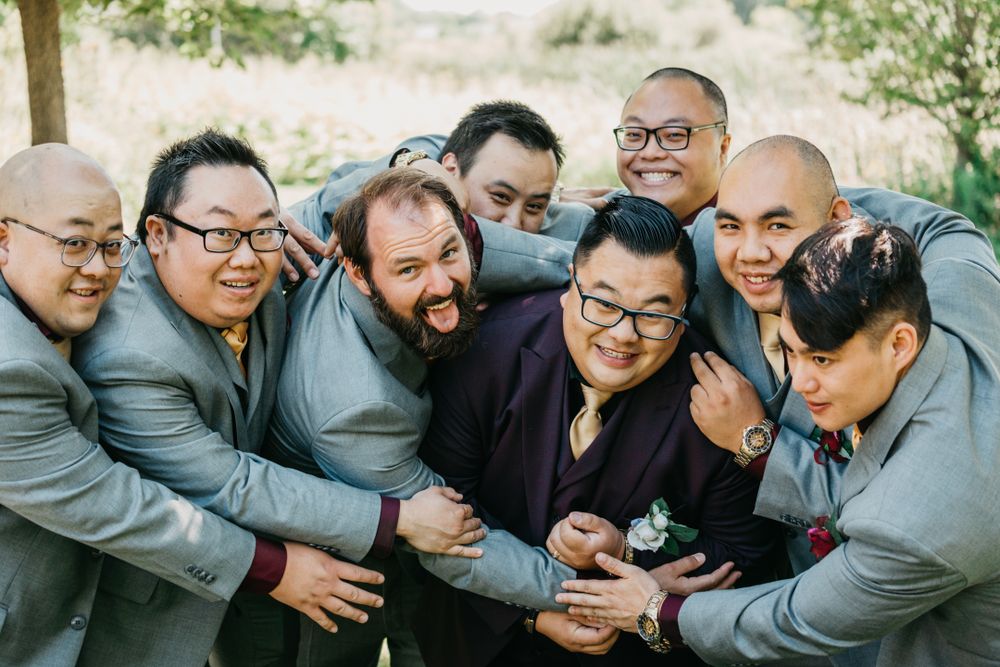 Group of groomsmen in gray suits posing playfully together for wedding photos.