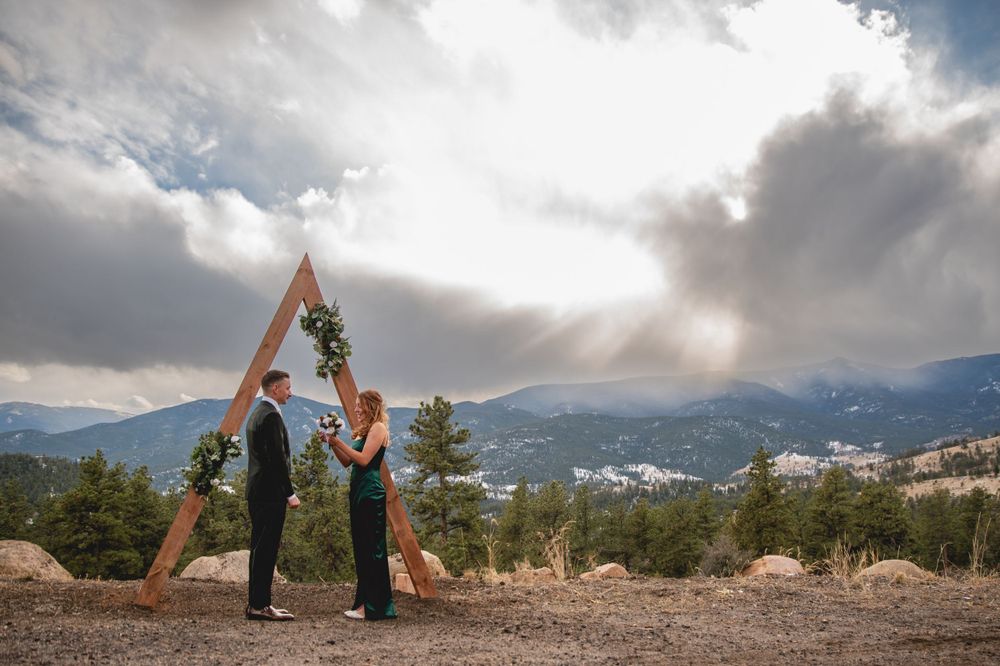 Outdoor ceremony site features wooden triangle arch against dramatic mountain landscape.