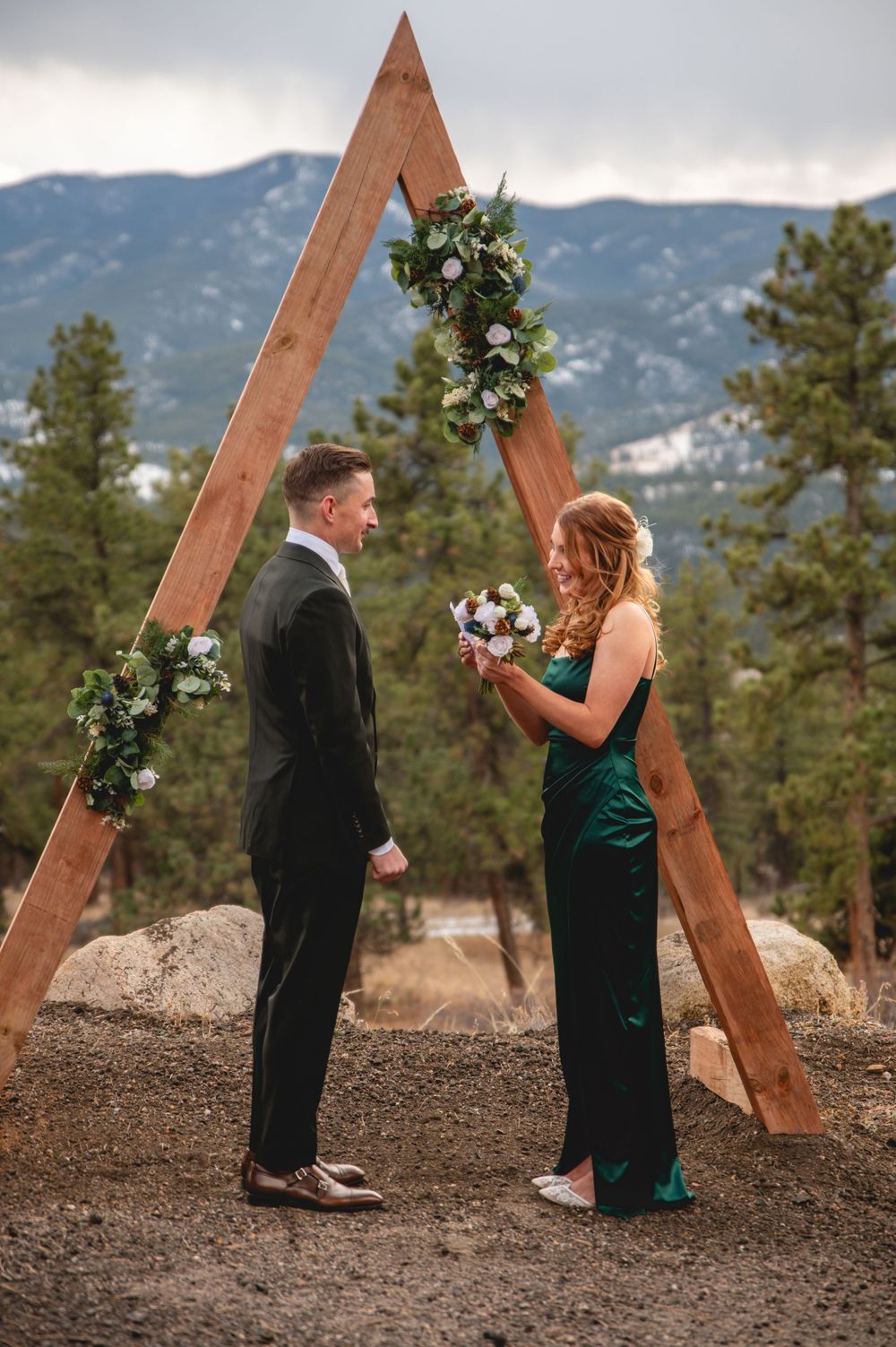 Elegant mountain wedding ceremony with wooden triangle arch and floral decorations.