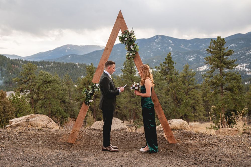 Mountain wedding ceremony featuring wooden triangle arch and dramatic cloudy sky.