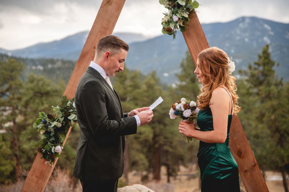 Intimate mountain ceremony with couple exchanging vows under decorated wooden arch.