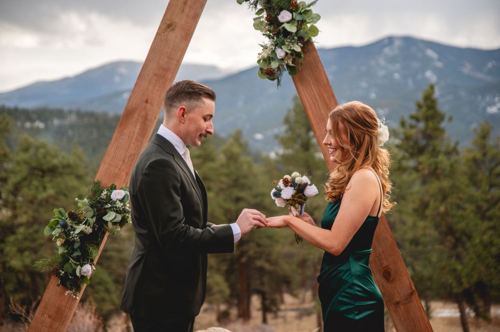 Exchange of rings during mountain ceremony beneath wooden triangle arch.