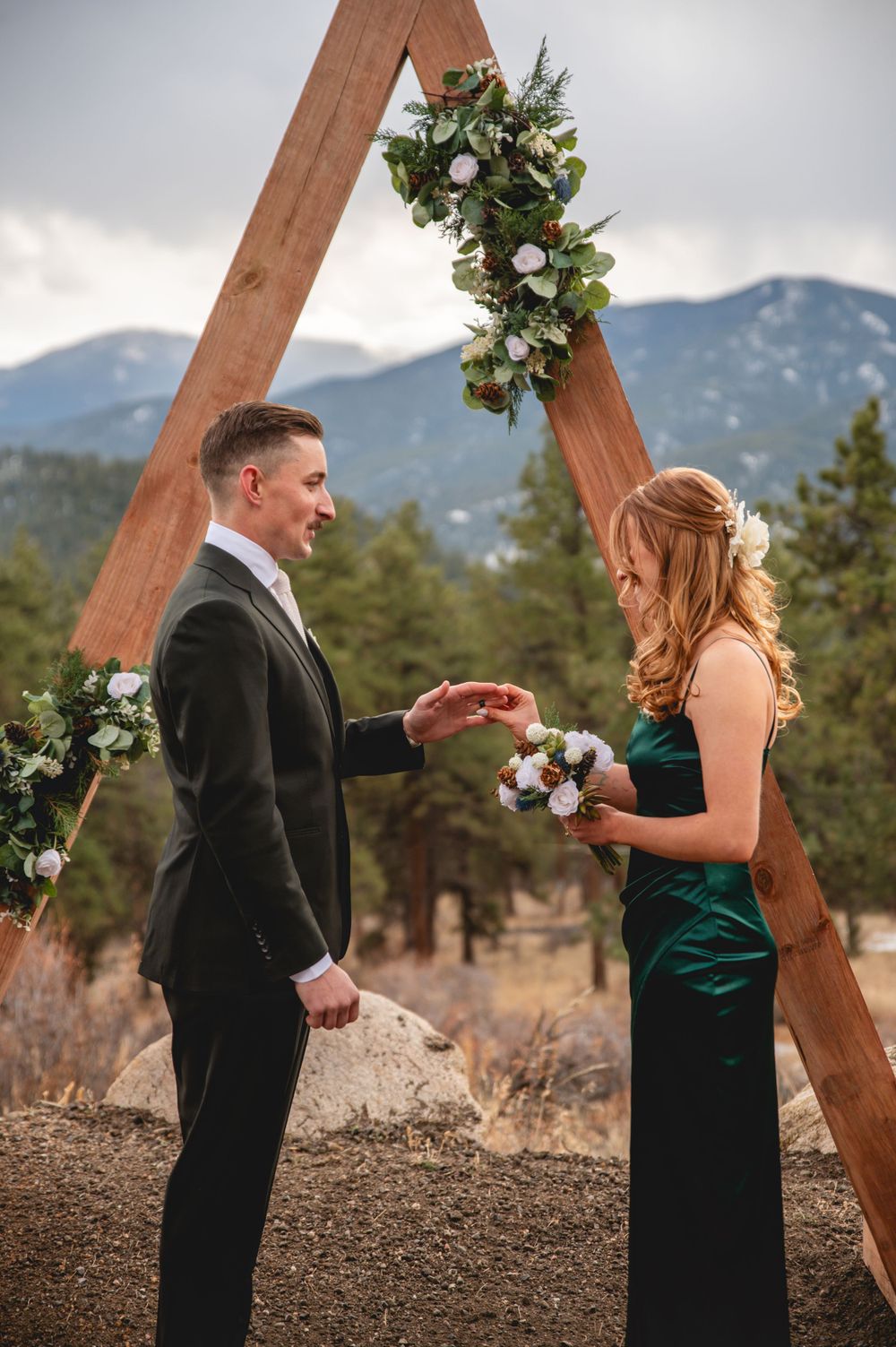 Mountain wedding ceremony with wooden arch decorated with white flowers and greenery.