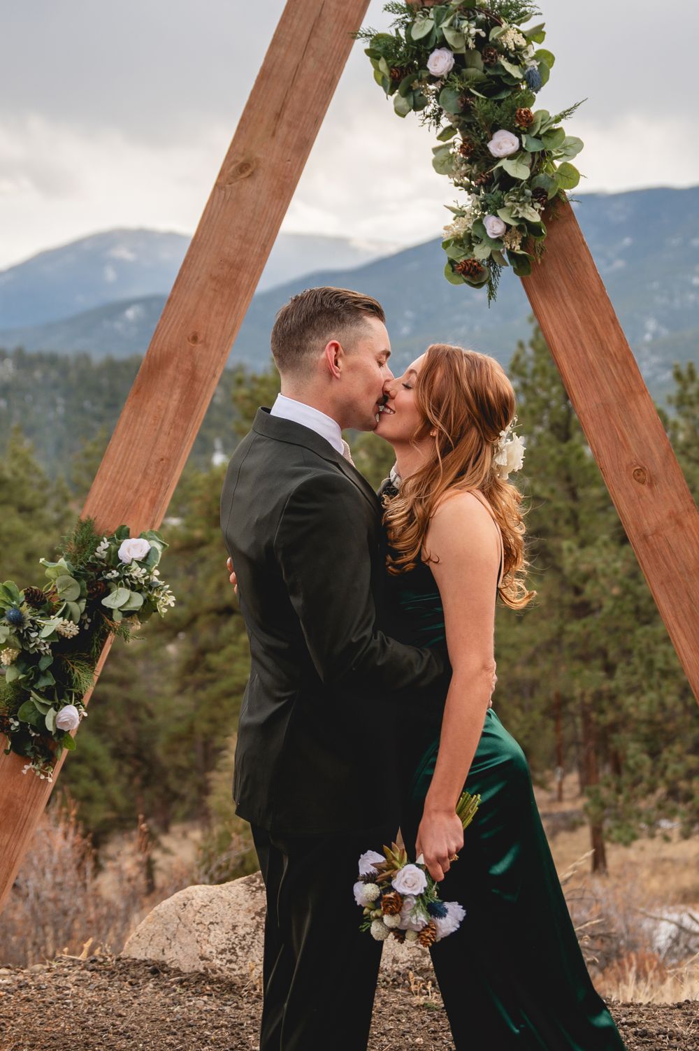 Romantic moment captured under wooden triangle arch in mountain setting.