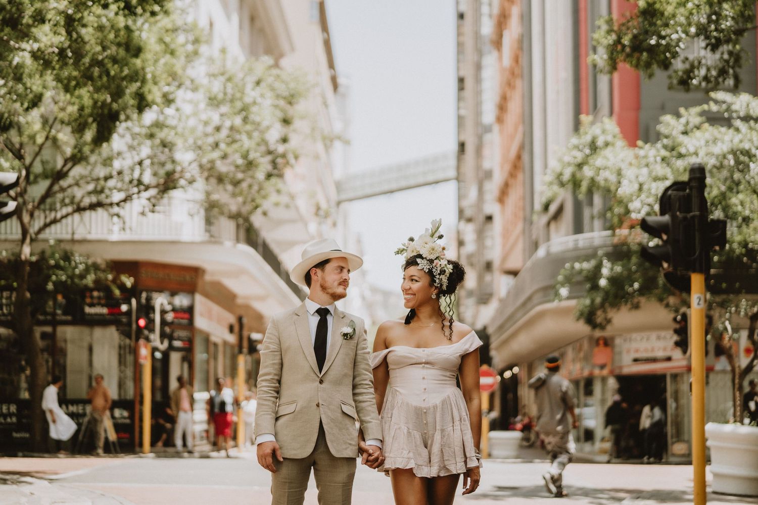 A couple in casual wedding attire share a joyful moment together on a sunny city street.