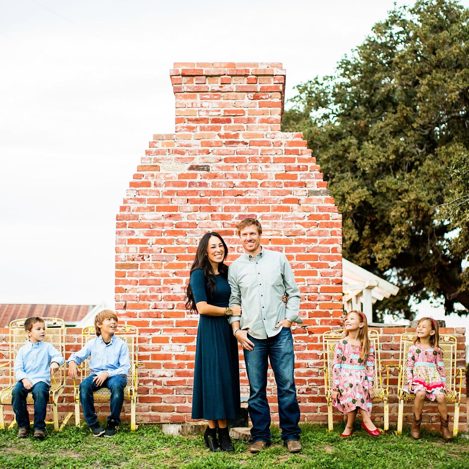 Family portrait in front of brick chimney with children sitting on wooden benches.